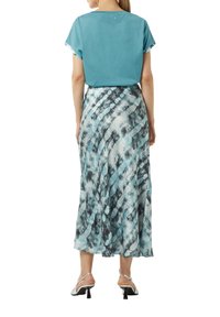 Turkusowa bawełniana bluzka z krótkimi rękawami połączona z długą, zwiewną spódnicą w niebiesko-szarym wzorze tie-dye; czarne sandały na obcasie.