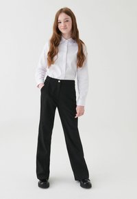 Biała, długosleeve koszula zapinana na guziki z kołnierzykiem, w połączeniu z czarnymi eleganckimi spodniami z przodu, które mają kieszeń i złote guziki.