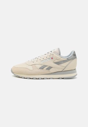 Baskets en cuir beige et daim avec des accents gris, bout rond, fermeture à lacets et épaisse semelle en caoutchouc gris. Présente le logo Reebok sur le côté.