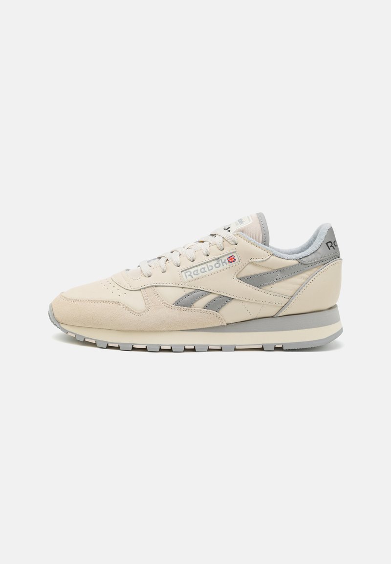 Beige läder- och mockaskor med grå detaljer, rund tå, snörningsstängning och en tjock grå gummisula. Har Reebok-logotyp på sidan.