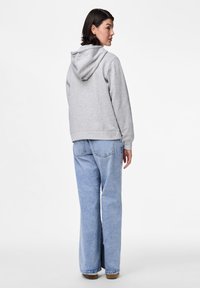 Sivi dukserica s kapuljačom opuštenog kroja, prikazana s leđa; u kombinaciji s svijetloplavim širokim trapericama i suptilnim detaljima na džepovima.