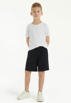 Weißes Baumwoll-T-Shirt kombiniert mit marineblauen Shorts; die Shorts sind mit einem elastischen Bund, zwei vorderen Taschen und einer lockeren Passform ausgestattet; das Modell trägt weiße Sneakers.
