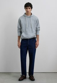 Sudadera gris con cordones, jeans azul oscuro y zapatos marrones con cordones. El conjunto presenta un ajuste relajado y texturas suaves.