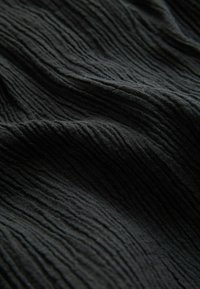 Tessuto nero con texture, caratterizzato da righe verticali prominenti, che presenta un aspetto leggermente spiegazzato e una finitura morbida e opaca.