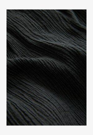 Zwart textiel met een opvallend verticale ribbels, vertonend een licht gekreukt uiterlijk en een zachte, matte afwerking.