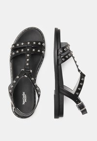 Sandali neri in pelle con più cinghie e borchie argentate. Presentano una cinghia alla caviglia regolabile e una suola piatta per il comfort. Design minimalista.