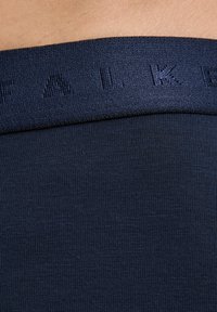 Fascia in tessuto elasticizzato blu navy con lettering in rilievo "FALK". Il materiale appare liscio con una texture a coste sotto la fascia.