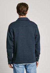 Mörk marinblå sweatshirt med krage, lång ärm och textil med struktur. Lager på ett rutigt skjorta vid fållen, har knäppta manschetter.