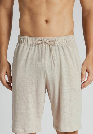 Mandlig torso iført beige snøreshorts, der viser talje, hænder og øvre lår mod en ensfarvet grå baggrund.