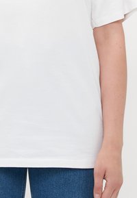 Vit bomull T-shirt med korta ärmar, som har en avslappnad passform och en slät yta. Den nedre kanten är något böjd.