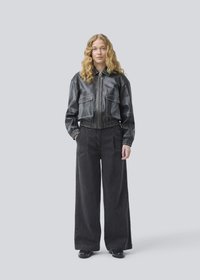Veste en cuir noir, courte, avec fermeture éclair à l'avant, deux poches poitrine et taille élastique, associée à un pantalon en denim noir à jambes larges. Chaussures noires.