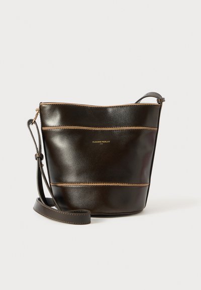Sac seau en cuir marron foncé avec des coutures contrastantes. Dispose d'une fine bandoulière et d'un logo doré à l'avant. Design simple et fonctionnel.