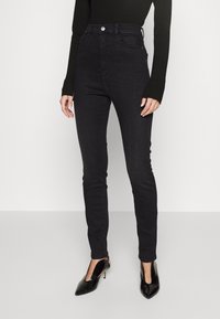High-waisted black skinny jeans made of denim, featuring a classic five-pocket design and subtle stitching, paired with black pointed heels.