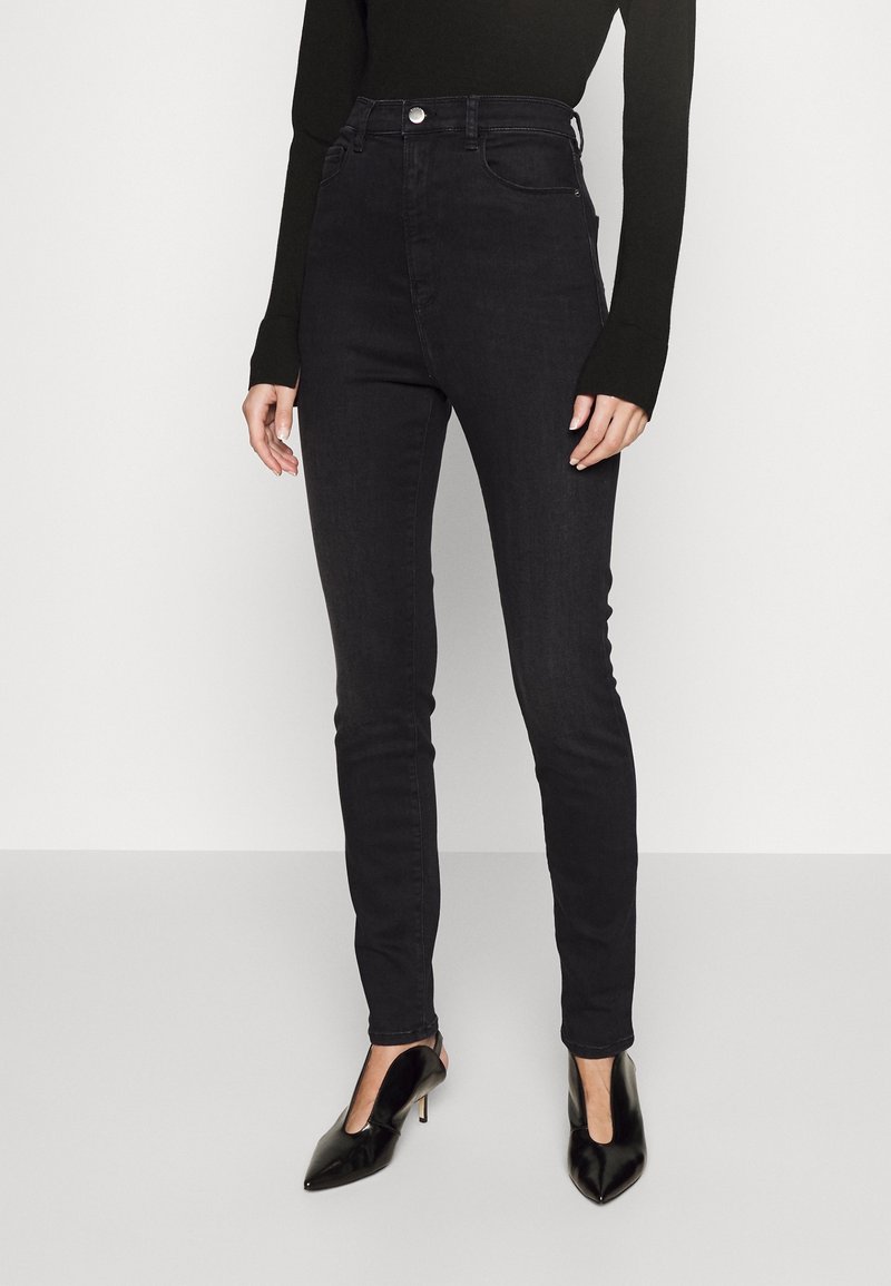 High-waisted black skinny jeans made of denim, featuring a classic five-pocket design and subtle stitching, paired with black pointed heels.
