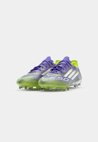 Ghete de fotbal violet și verde lime, cu un design texturat, închidere cu șireturi și cuie transparente. Au branding alb și o formă elegantă.