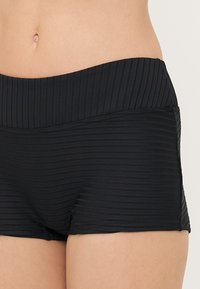 Shorts de bain noirs avec un design texturé en côtes, présentant une taille large et une coupe ajustée. Tissu lisse avec un subtil brillant.