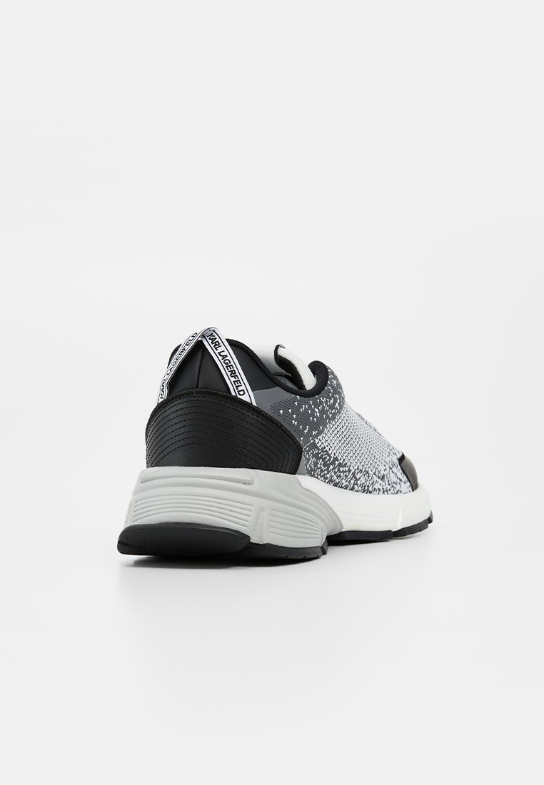 Zapatilla de punto gris y negra con suela blanca gruesa, soporte negro en el talón y lengüeta con la etiqueta "KARL LAGERFELD" en la parte trasera.