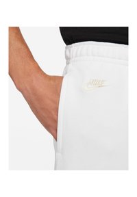 Vita joggerbyxor med elastisk midja, sidofickor och en guldbroderad Nike-logotyp på låret. Mjuk tyg med en slät yta.