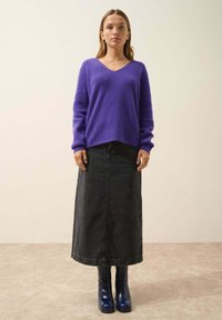 Fioletowy sweter dzianinowy z dekoltem w kształcie litery V, w połączeniu z długą czarną spódnicą dżinsową i niebieskimi botkami na obcasie do kolan. Prosty, zorganizowany fason.