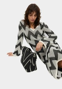 Abito a maglia bianco e nero con motivo a zigzag, caratterizzato da scollo a V e maniche lunghe. Nelle vicinanze, una borsa nera testurizzata con accenti bianchi.