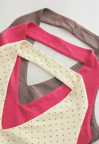 Trois hauts sans manches pliés avec encolures en V, en marron, rose et crème, avec des motifs de cœurs noirs sur tissu crème.