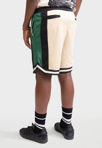 Twee-kleurige shorts met een beige basis, groene en zwarte zijpanelen, zwarte bies en zijzakken. Gecombineerd met zwarte sneakers en gestreepte sokken.