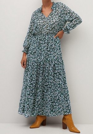 Vestido largo floral en verde oscuro con flores blancas y azules, mangas largas, cintura elástica y dobladillo con volantes en capas; combinado con botines color canela.