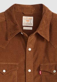 Bruine corduroy overhemd met een puntkraag, witte drukknoopjes, twee borstzakken en een rode Levi's label op de linkse zak.