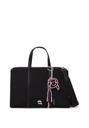 Černá obdélníková taška na rameno se dvěma uchy, odnímatelným polstrovaným řemínkem a růžovou klíčenkou s kreslenou tváří zavěšenou na jednom uchu.