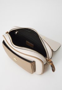 Beige og lys kremfarget skinnveske med svart innvendig. Har glidelåslukking på toppen, en frontlomme med klaff, og detaljer i gulltone.