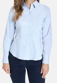 Light blue button-up shirt with long sleeves, a pointed collar, and a curved hem. Made from smooth fabric; features button accents.