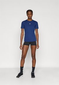 Camiseta deportiva azul marino de manga corta con logotipo en el pecho, combinada con pantalones cortos negros con franjas blancas en los costados y zapatillas negras.