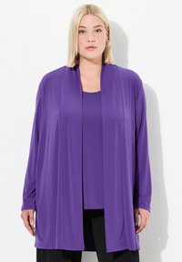 Lila geschichtetes Oberteil aus einem glatten, leichten Stoff. Das Design umfasst lange Ärmel und eine offene Vorderseite, kombiniert mit einem passenden Top darunter.