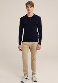 Polo de manga larga azul marino con una tapeta de tres botones, combinado con chinos beige claros y zapatillas grises. Tejido suave y ligero.