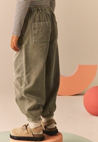 Hellgrüne Cordhosen mit elastischem Bund, tiefen Taschen und gerafften Bündchen. Getragen mit beigen Slippern und weißen Socken.