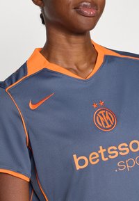 Grå sportströja med orange accenter, som har en v-halsdesign, Nike-logotyp och broderad lagmärke. Texten lyder "betsson.sport."
