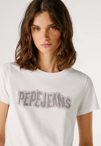 Camiseta de algodón blanca con un diseño texturizado que presenta las palabras "PEPE JEANS" en adornos brillantes en la parte frontal. Mangas cortas.