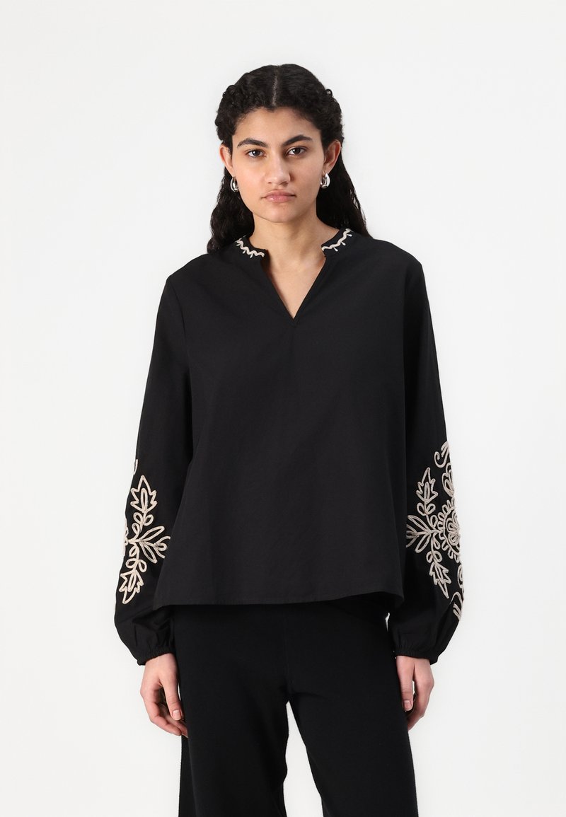 Blusa nera con scollo a V, maniche lunghe e intricate ricami color crema sulle maniche. Realizzata in un tessuto morbido, vestibilità comoda.