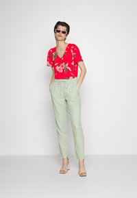 Top floral vermelho com mangas curtas e decote em V, combinado com calças verde-claro de perna tapered, com cintura elástica e cordão.