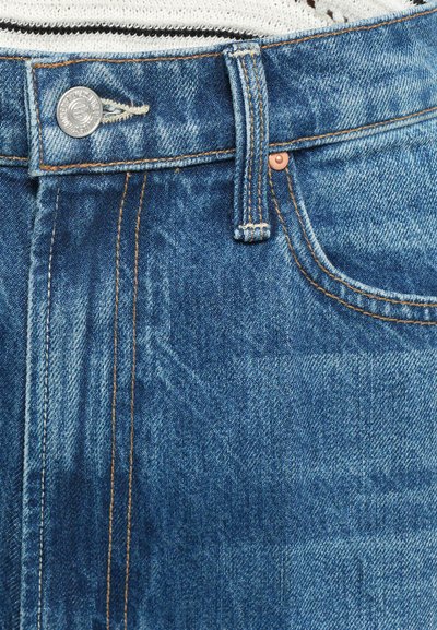 Gros plan sur la taille d'un jean en denim bleu, bouton, passant de ceinture et poche avant avec des coutures visibles et une texture de tissu.