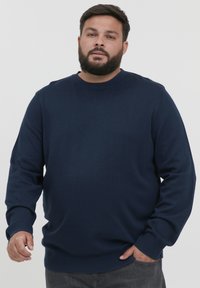 Suéter de punto azul marino con cuello redondo, puños y dobladillo acanalados. Textura suave, corte casual y diseño simple sin patrones.
