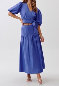 Top blu con maniche a sbuffo e gonna a vita alta coordinata con dettaglio arricciato. Realizzato in tessuto leggero, con una texture liscia.