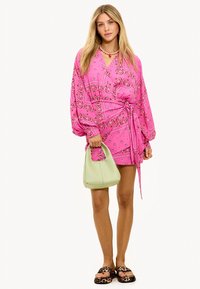 Robe rose avec motif cachemire, manches longues et ceinture à nouer. Accessoirisée d'un sac vert clair et de sandales à enfiler à motif léopard.