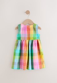 Kolorowa sukienka w kratę z jaskrawymi odcieniami różu, zieleni, niebieskiego i żółtego, bez rękawów, z marszczonym dołem, zawieszona na drewnianym wieszaku.