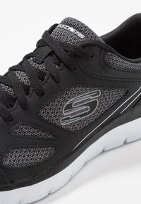 Black and gray Skechers sneaker with knitted fabric, black laces, and white sole, shown from a close-up angle.