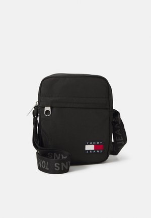 Schwarze Nylon-Crossbody-Tasche mit Reißverschluss, ausgestattet mit einem Logopatch und einem verstellbaren Riemen, auf dem der Markenname in Grau zu sehen ist.