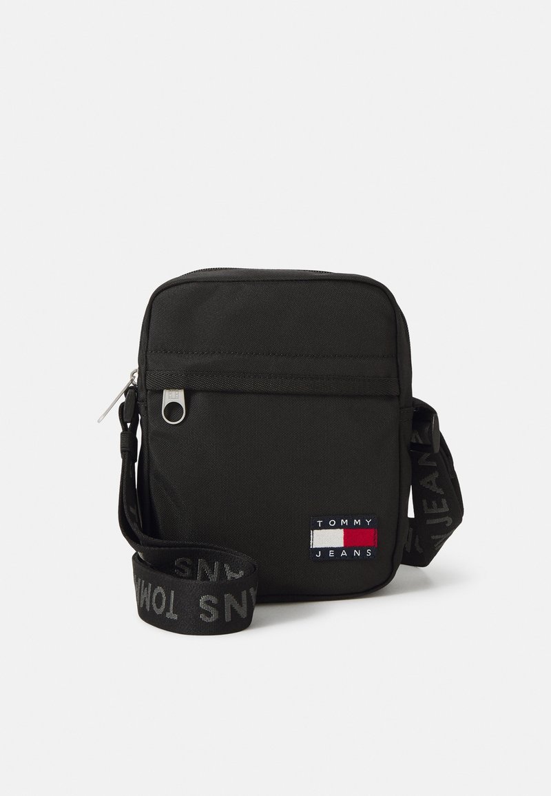 Schwarze Nylon-Crossbody-Tasche mit Reißverschluss, ausgestattet mit einem Logopatch und einem verstellbaren Riemen, auf dem der Markenname in Grau zu sehen ist.
