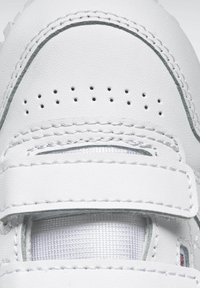 Hvite lær sneakers med teksturert overflate, som har en borrelåsrem, små perforeringer og dekorativ grå søm.