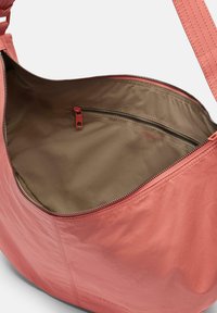 Torba na ramię w koralowo-różowej skórze, z gładkim wykończeniem, zamykana na zamek błyskawiczny i beżowym, materiałowym wnętrzem z małą kieszonką na zamek.