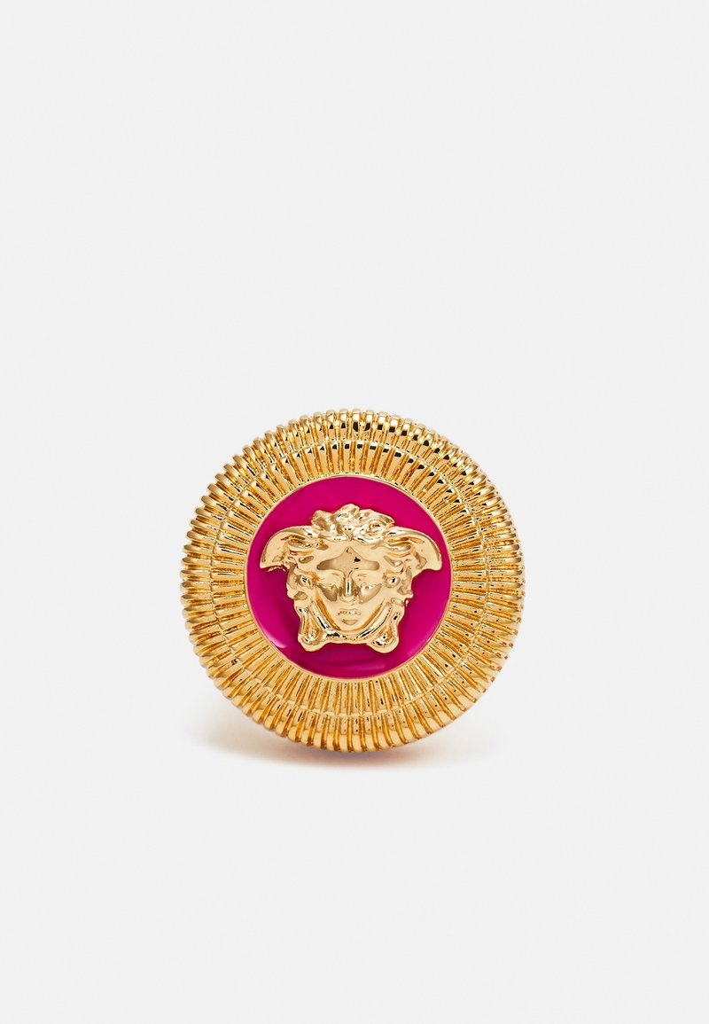 Bouton rond en or avec des bords striés, présentant un emblème de tête de Méduse dorée sur un fond circulaire rose vif.